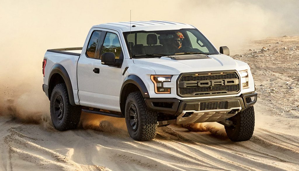 A white Ford F-150 Raptor kicks up some dirt.