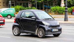 A gas-powered Smart car drives down the street